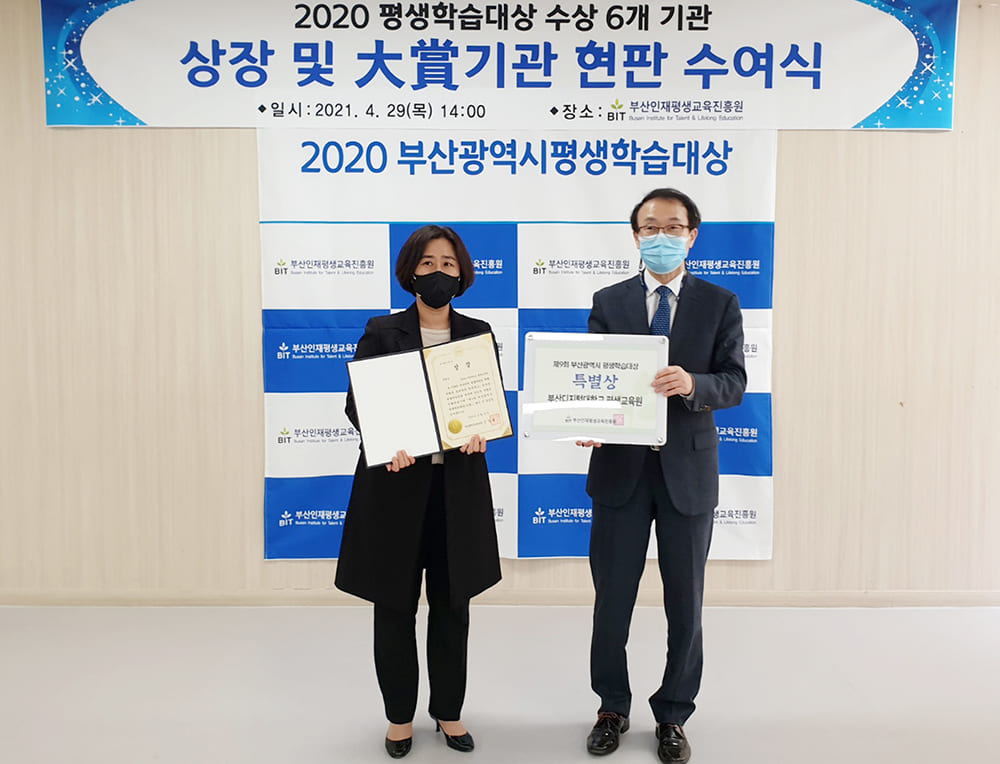 2020 평생학습대상 수상 6개 기관 상장 및 대상기관 현판 수여식, 2020 부산광역시평생학습대상 현수막배경으로. 엄세진평생교육원장은 상장을 펼쳐들고, 부산인재평생교육원장은 현판을 들고 찍은 기념사진. 코로나 19지침에 따라 마스크를 쓰고있다. 